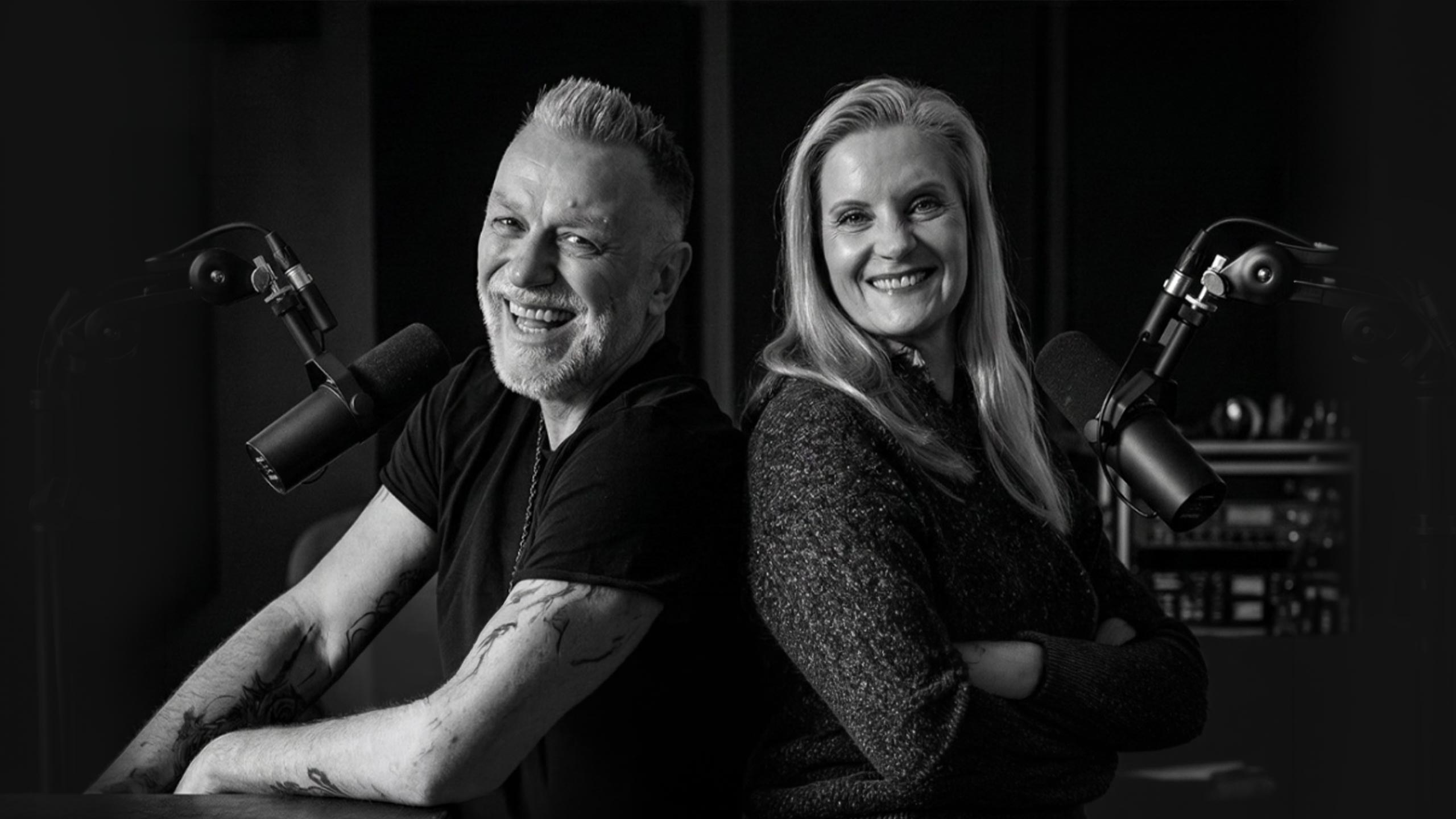 Zwei Podcast-Moderatoren im Studio mit Mikrofonen, lächelnd beim Sprechen im Aufnahmeraum